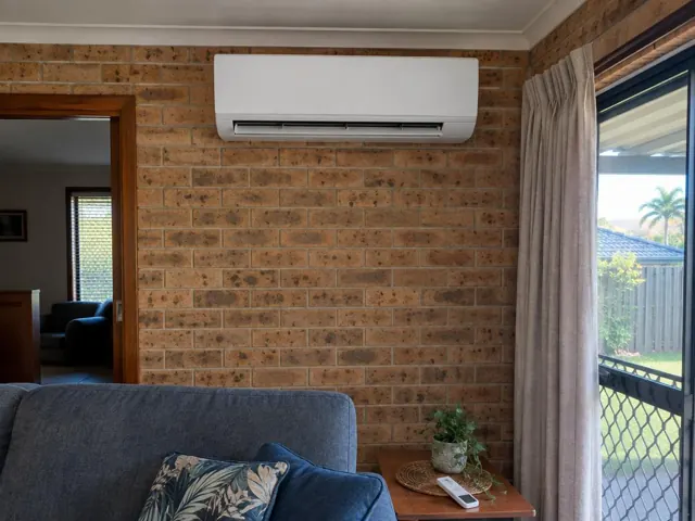 Brick living room wall with a mounted split system above a doorway and curtained window in Coolangatta