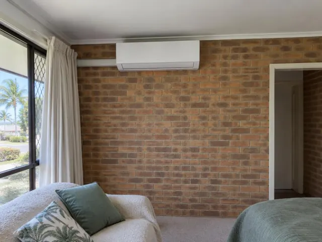 Wall-mounted split system on a brick feature wall in a bedroom with window curtains in Tugun